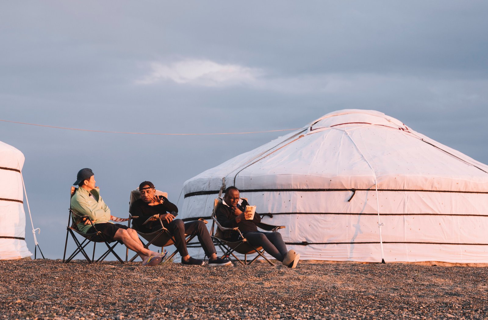 Travellers sitting out in camp chairs beside white gers under an evening sky