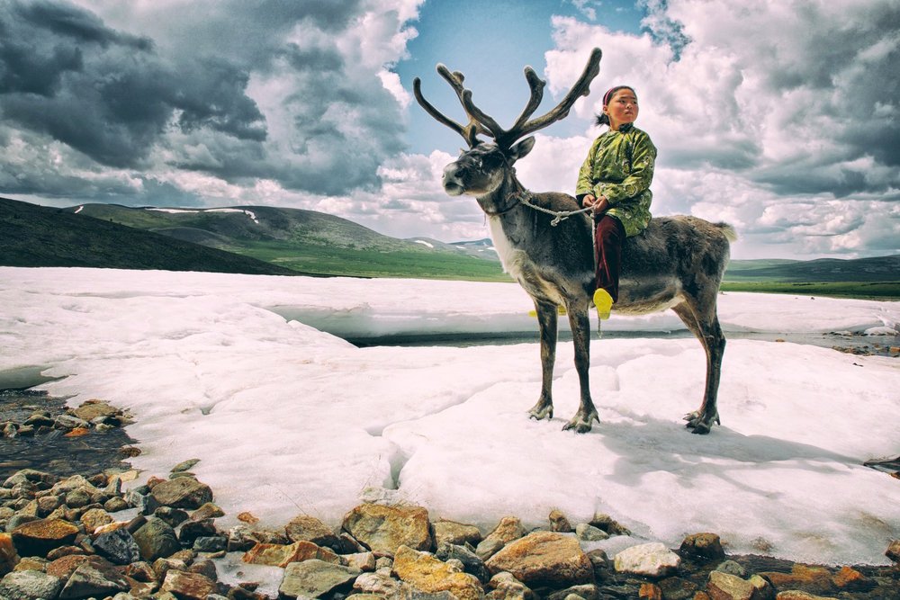 Tsaatan herder on a reindeer below dark cloud in the Ulaan Taiga